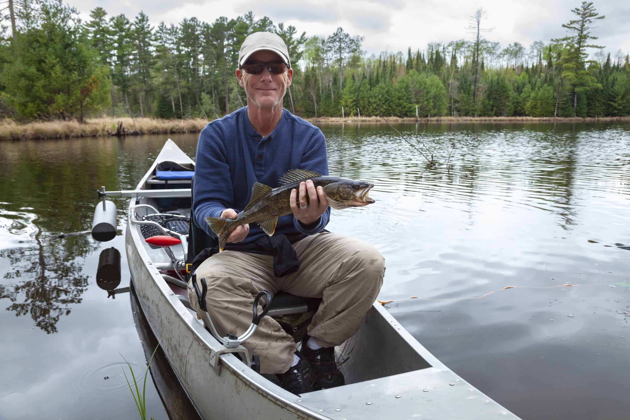 Smiling fisherman sitting in a canoe on a Minnesota lake holds up a walleye